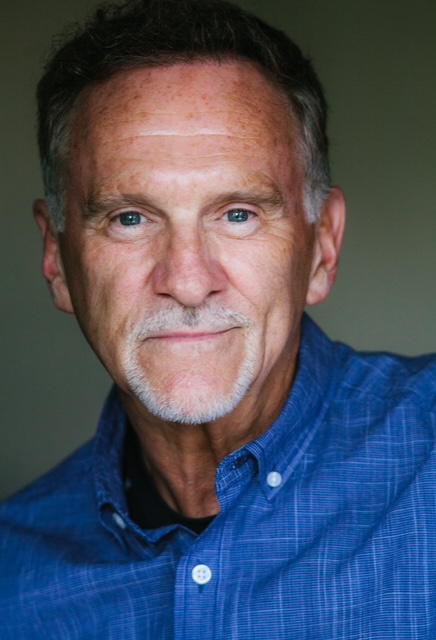 Close-up headshot of Gregory F. smiling and wearing a blue blazer over a collared shirt.